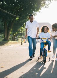 man standing beside his wife teaching their child how to ride bicycle
